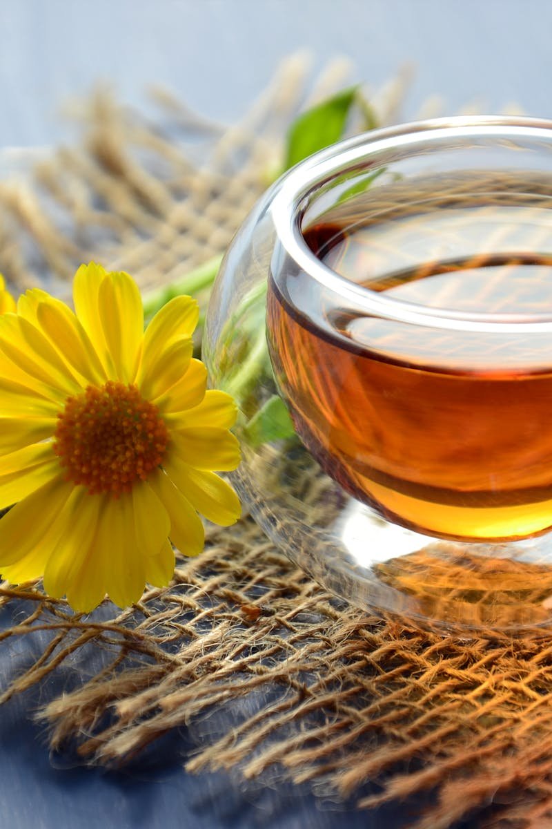 Glass cup of herbal tea with yellow flowers on a textured background.